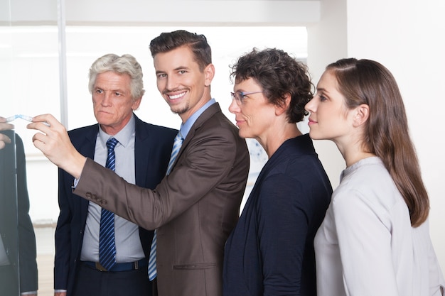 Smiling businessman drawing on flipchart for team