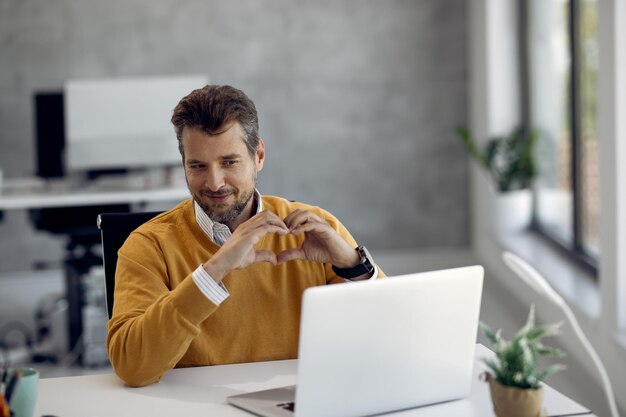 Smiling businessman internet dating and showing heart shape during a video call