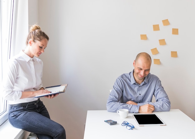 Smiling businessman looking at digital tablet with businesswoman looking at diary in the office