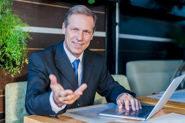 Smiling businessman making hand gesture with laptop over desk in restaurant