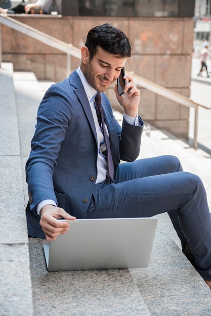 Smiling businessman speaking on phone and browsing laptop