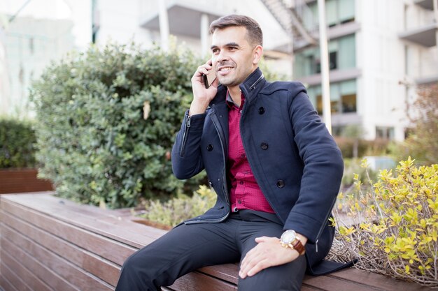 Smiling businessman talking on cellphone on bench