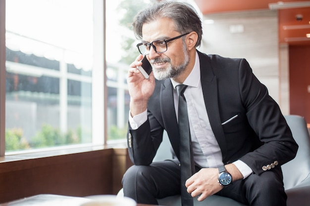 Smiling Businessman Talking on Smartphone in Lobby