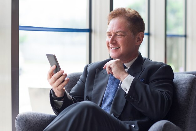 Улыбаясь бизнесмен, с помощью мобильного телефона в лобби