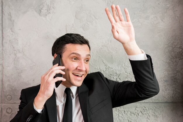 Smiling businessman waving with hand and chatting on phone