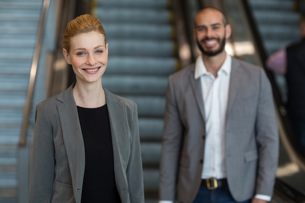 Smiling businesspeople with luggage standing in front of an escalator