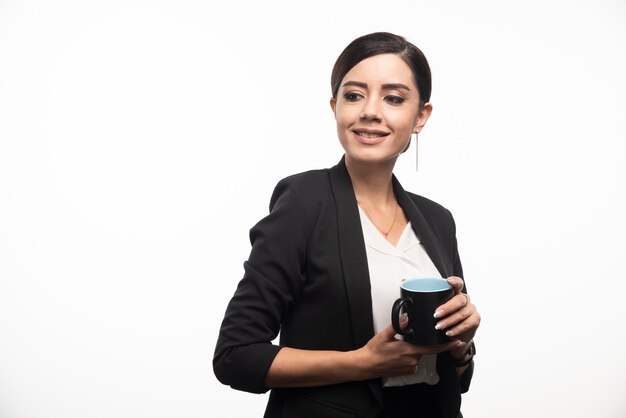 Smiling businesswoman holding cup on white wall.