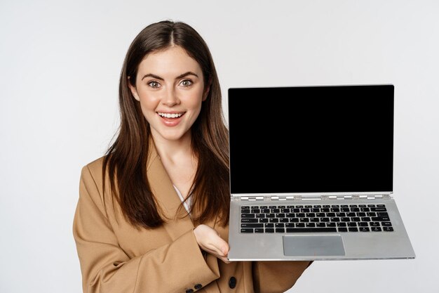 Smiling businesswoman, saleswoman showing laptop screen, demonstrating website, logo, standing against white background