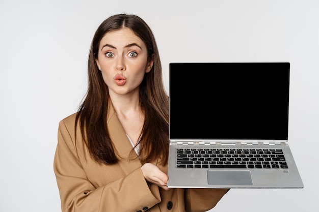 Smiling businesswoman, saleswoman showing laptop screen, demonstrating website, logo, standing against white background.