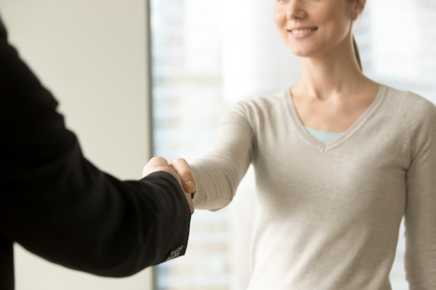 Улыбающаяся деловая женщина пожимает руку бизнесмену в офисе