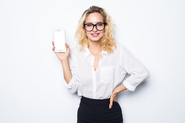 Smiling businesswoman showing blank smartphone screen over gray wall. Wearing in blue shirt and glasses.