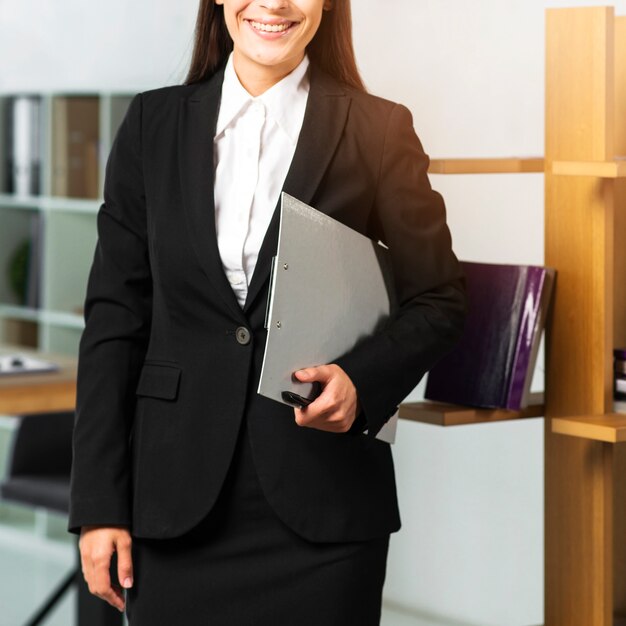 Smiling businesswoman standing in office holding clipboard