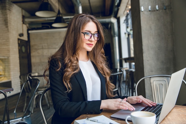 Free photo smiling businesswoman typing on laptop sitting in a cafe