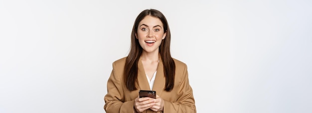 Donna di affari sorridente che utilizza l'app per smartphone sul telefono cellulare in piedi su sfondo bianco