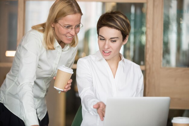 Smiling businesswomen discussing good online project result looking at laptop 