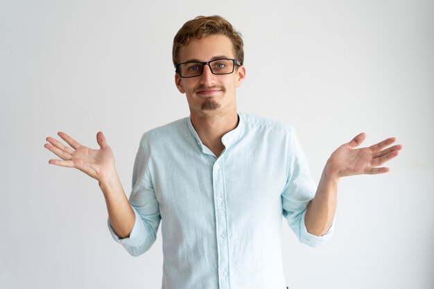 Smiling careless blonde guy showing do not know gesture.