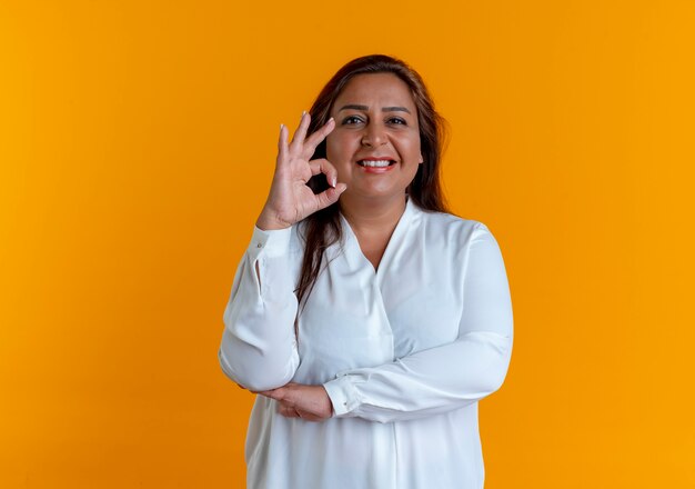 Smiling casual caucasian middle-aged woman showing okey gesture isolated on yellow wall