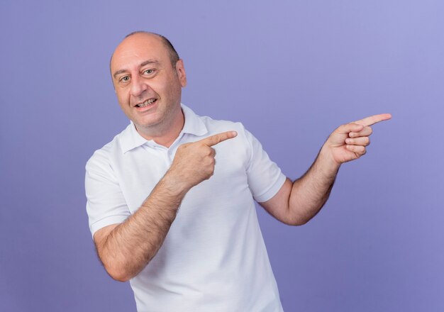 Smiling casual mature businessman pointing at side isolated on purple background