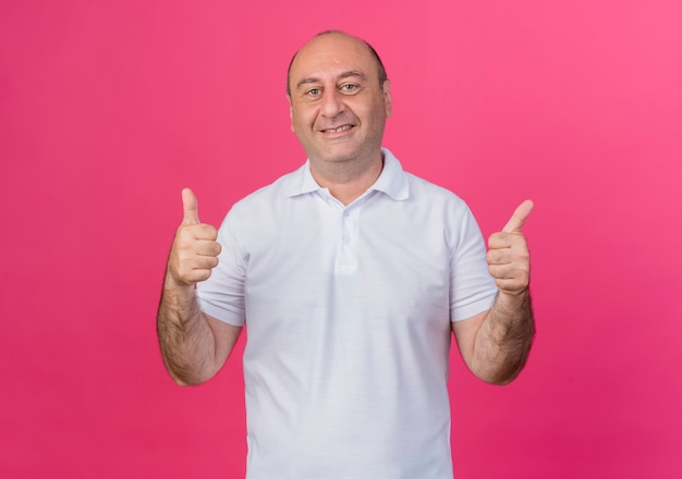 Smiling casual mature businessman showing thumbs up isolated on pink background with copy space