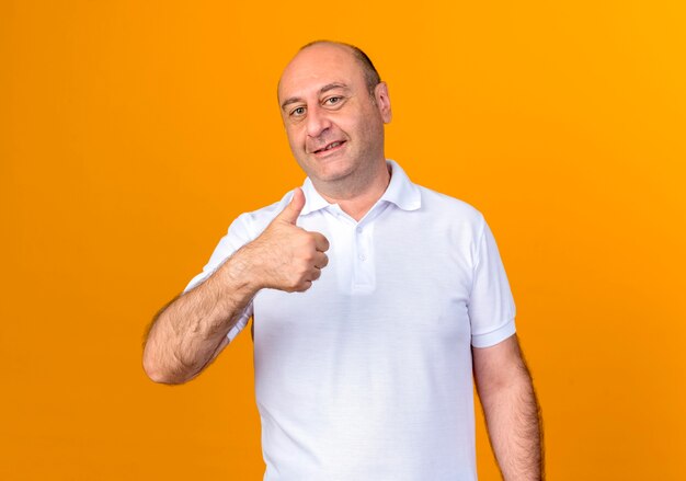 Smiling casual mature man his thumb up isolated on yellow wall