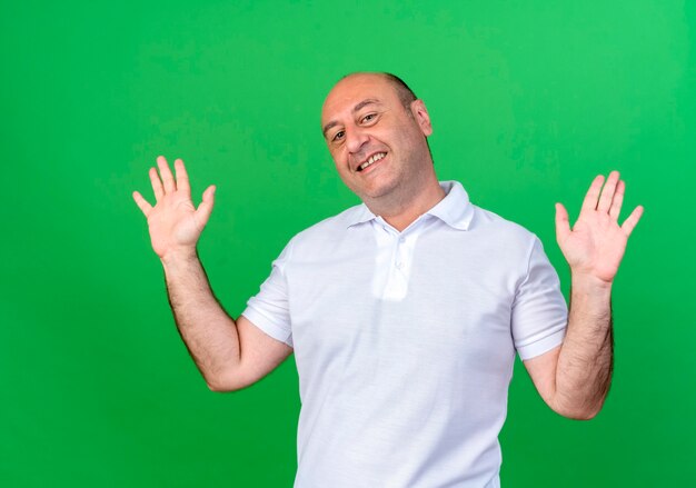 Smiling casual mature man spreads hands isolated on green wall