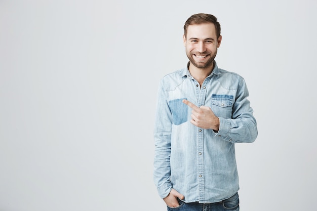 Smiling caucasian bearded man pointing finger left, advertising