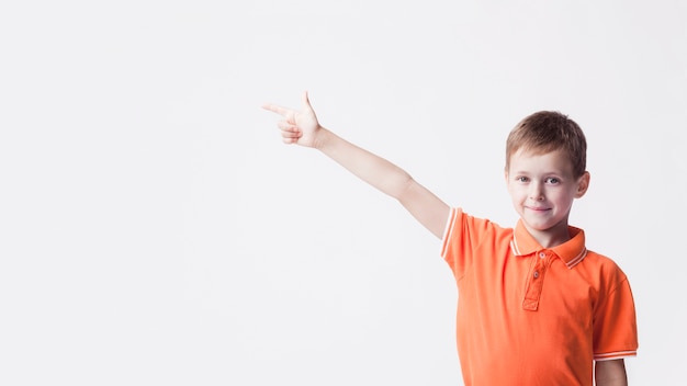 Smiling caucasian boy pointing index finger at side on white backdrop