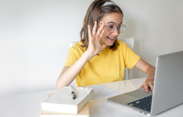 Foto gratuita sorridente ragazza caucasica che ha una videochiamata in classe remota utilizzando il computer portatile