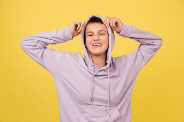 Smiling. Caucasian girl's portrait isolated on yellow studio background with copyspace for ad. Beautiful female model in hoodie. Concept of human emotions, facial expression, sales, ad, fashion.