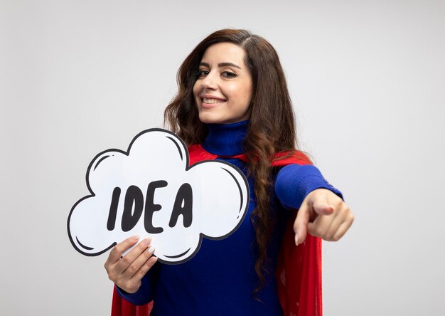 Улыбающаяся кавказская девушка-супергерой с красной накидкой держит пузырь идей