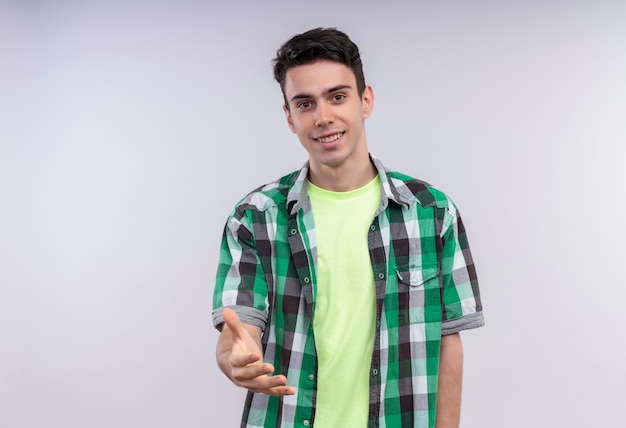 Smiling caucasian young guy wearing green shirt held out hand to camera on isolated white background