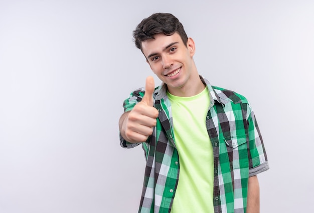 Sorridente ragazzo giovane caucasico indossando la camicia verde il pollice in alto su sfondo bianco isolato