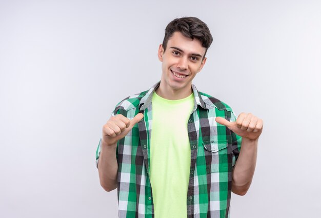 Улыбающийся кавказский молодой парень в зеленой рубашке показывает себя на изолированном белом фоне
