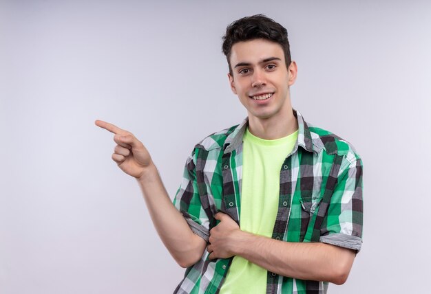 Smiling caucasian young guy wearing green shirt points to side on isolated white background