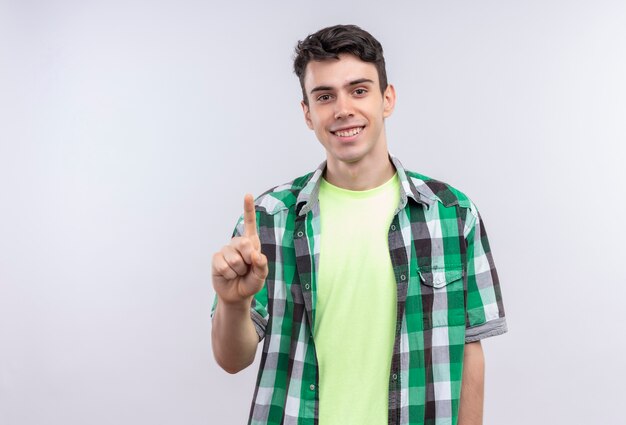 Il giovane ragazzo caucasico sorridente che porta la camicia verde indica su fondo bianco isolato