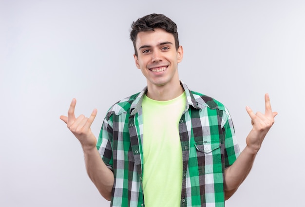 Улыбающийся кавказский молодой парень в зеленой рубашке показывает козий жест обеими руками на изолированном белом фоне