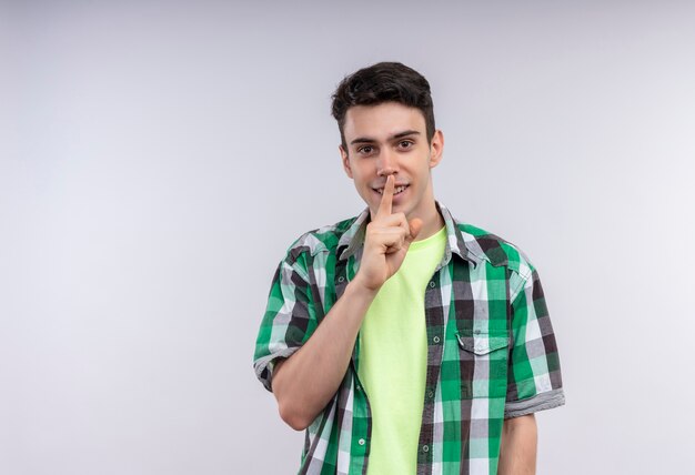 Smiling caucasian young guy wearing green shirt showing silence gesture on isolated white background