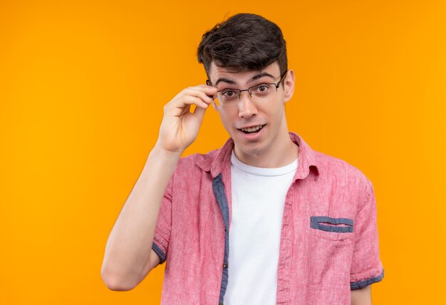 Smiling caucasian young guy wearing pink shirt in glasses on isolated orange background