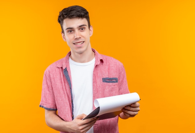 Smiling caucasian young guy wearing pink shirt holding clipboard on isolated orange background