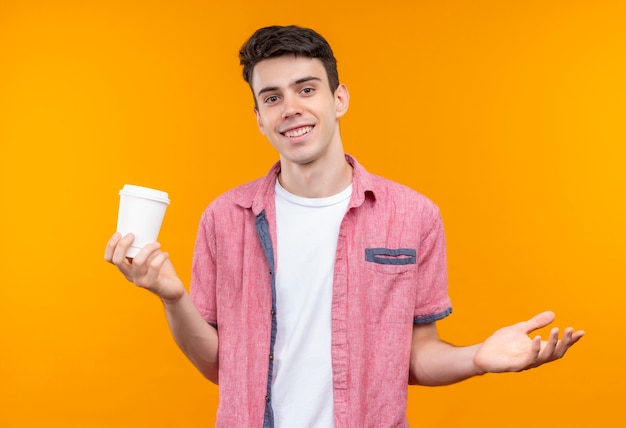 커피 한잔 들고 분홍색 셔츠를 입고 웃는 백인 젊은 남자가 고립 된 오렌지 배경에 손을 제기