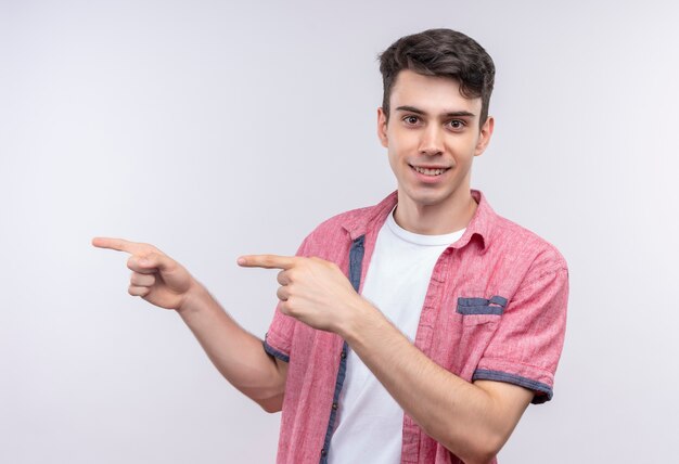 Smiling caucasian young guy wearing pink shirt points at side with both hands on isolated white background