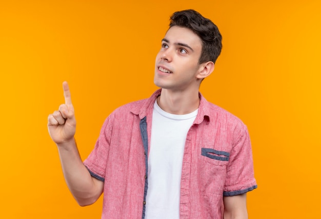Free photo smiling caucasian young guy wearing pink shirt points to up on isolated orange background
