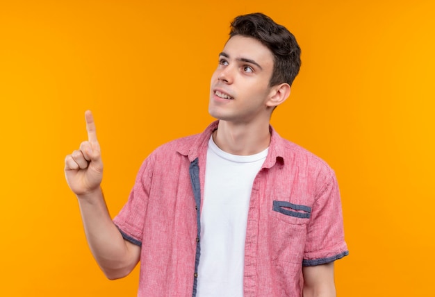 Foto gratuita il giovane ragazzo caucasico sorridente che porta la camicia rosa punta verso l'alto su fondo arancio isolato