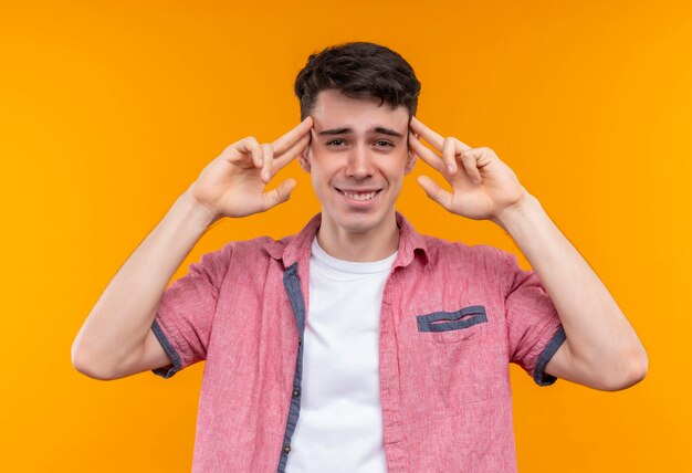 Smiling caucasian young guy wearing pink shirt put his fingers on forehead on isolated orange background