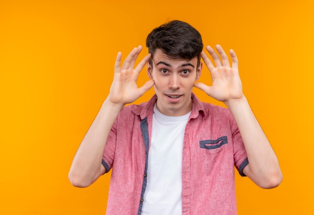 Smiling caucasian young guy wearing pink shirt put his hands around face on isolated orange background
