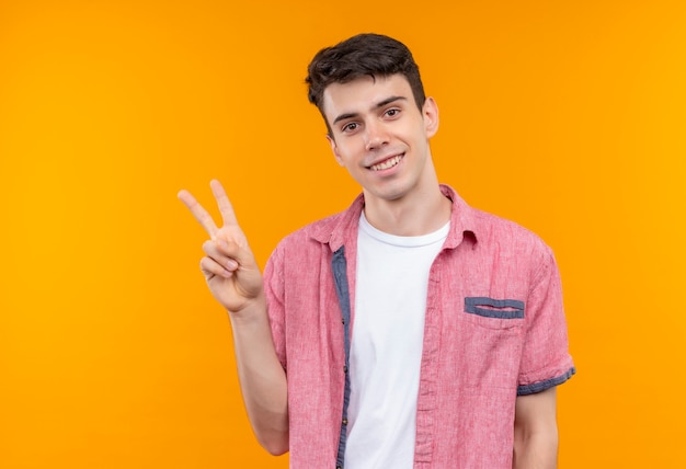Smiling caucasian young guy wearing pink shirt showing peace gesture on isolated orange background