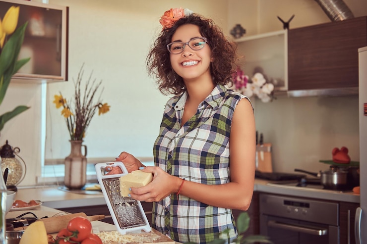 Бесплатный Фотография улыбающаяся очаровательная кудрявая латиноамериканка готовит на своей кухне. натираем сыр на терке.