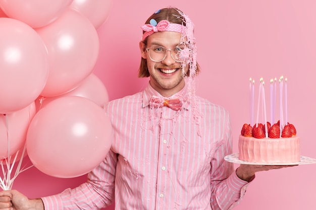 Free photo smiling cheerful adult man smeared with serpentine spray enjoys birthday party celebrates anniversary