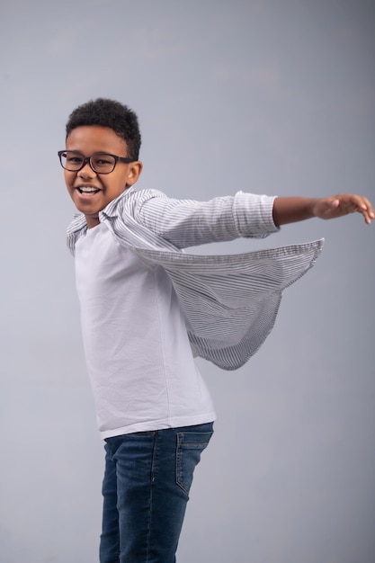 Smiling cheerful dark-skinned young boy in stylish spectacles getting ready to jump before the camera