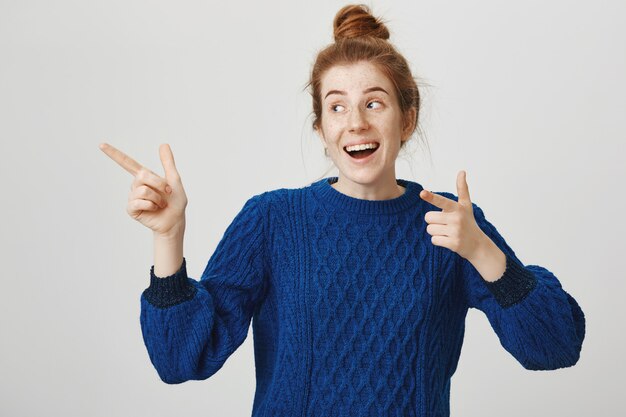 Smiling cheerful redhead girl showing advertisement, pointing left